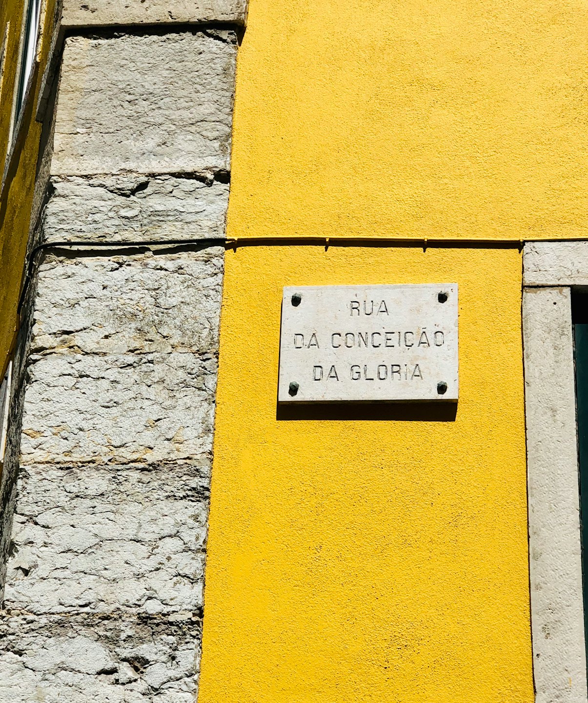 Street sign mounted on a textured yellow stone wall.